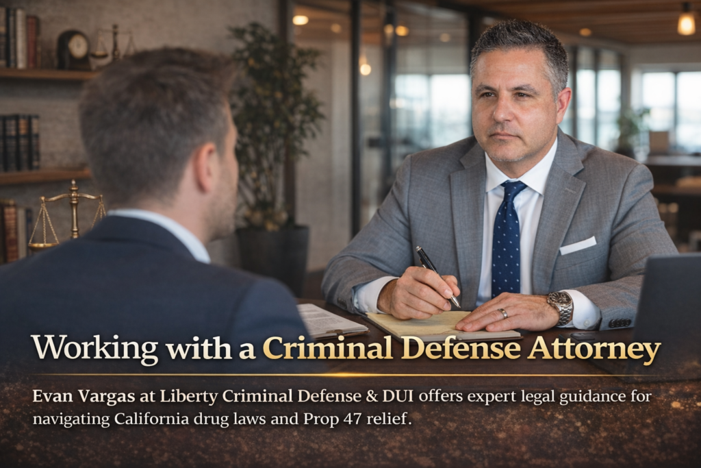 Image of attorney Evan Vargas in a professional office setting, seated at a desk and attentively consulting with a client, with law books and scales of justice visible in the background.