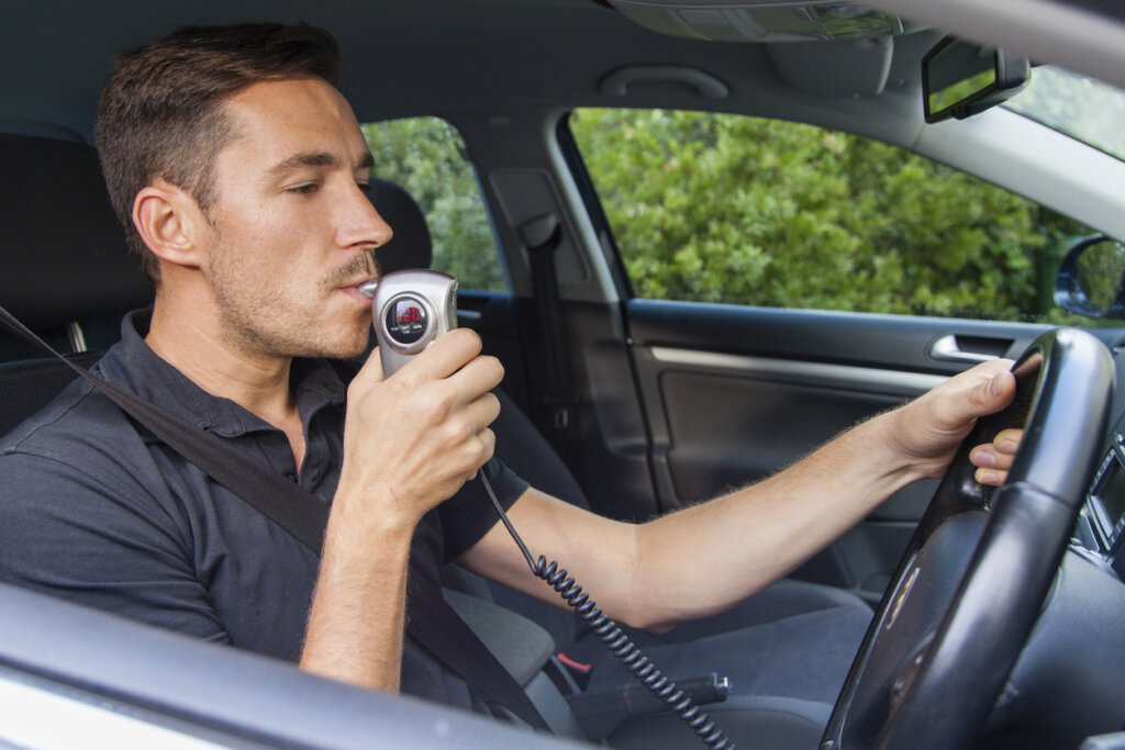 a man sitting in his car blowing into an ignition interlock device due to previous DUI charges